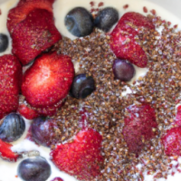 strawberries, blueberries, and raspberries mixed into a bowl with greek yogurt with some ground flaxseed mixed in
