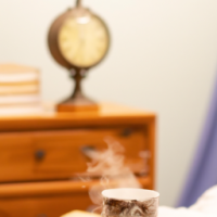 Show a mug with steaming tea sitting on a bedside table.