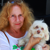 50 year old women with  long strawberry  blonde wavy  hair, blue eyes ,no wrinkles , no makeup with her  small white dog with her smiling