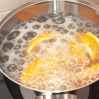 Saucepan of boiling water on a stove with orange peel infusing